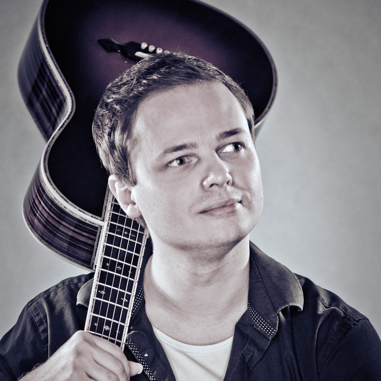 Carsten Langner in einem Fotostudio, eine Akustikgitarre über der rechten Schulter, blickt nachdenklich zur Seite (Foto: b7UE, 2016)
